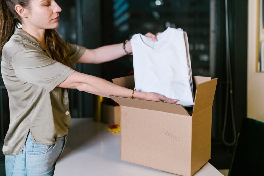 Adult woman placing t-shirts into a cardboard box, perfect for shipping or moving concepts.